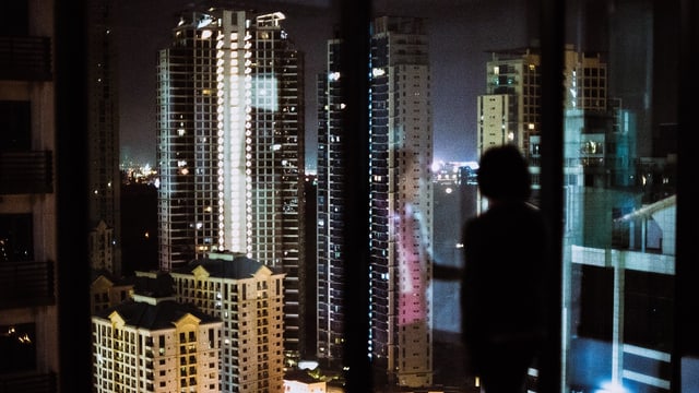 Eine Frau steht vor einen Fenster, vor ihr ist die nächtliche Skyline einer Grossstadt zu sehen. Eine Frau steht vor einen Fenster, vor ihr ist die nächtliche Skyline einer Grossstadt zu sehen.