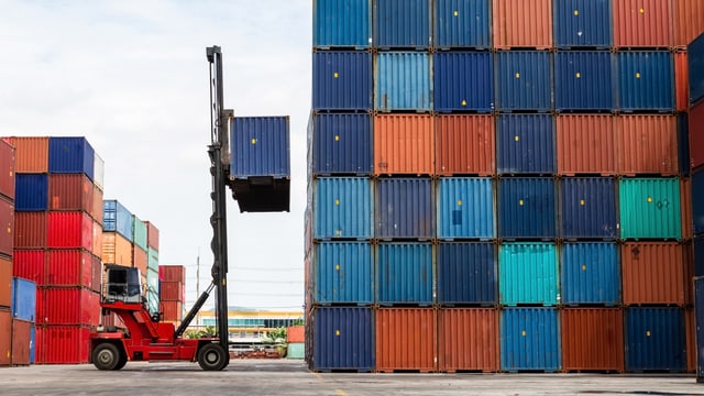 Ein Gabelstapler hebt einen Schiffscontainer auf einen Containerstapel. Ein Gabelstapler hebt einen Schiffscontainer auf einen Containerstapel.