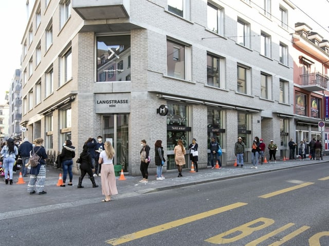Eine Schlange von Menschen steht entlang einer Strasse bis um eine Hausecke. Eine Schlange von Menschen steht entlang einer Strasse bis um eine Hausecke.
