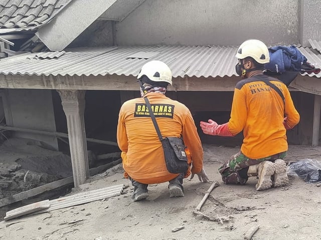 Petugas penyelamat sedang mencari seseorang yang terkubur di dekat sebuah rumah.