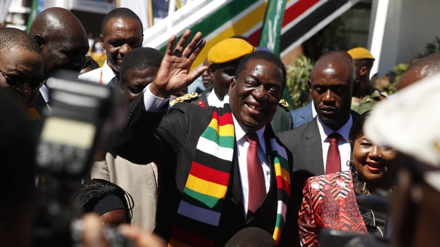 Mnangagwa zwischen anderen Menschen, er winkt in die Kamera. Mnangagwa zwischen anderen Menschen, er winkt in die Kamera.
