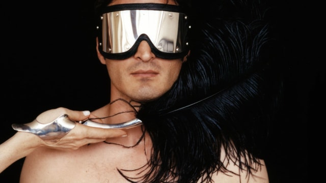 Ein Mann mit reflektierender Brille wird mit einer schwarzen Feder gestreichelt. Ein Mann mit reflektierender Brille wird mit einer schwarzen Feder gestreichelt.