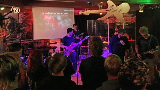 Konzert, im Hintergrund eine Leinwand mit Text. Konzert, im Hintergrund eine Leinwand mit Text.