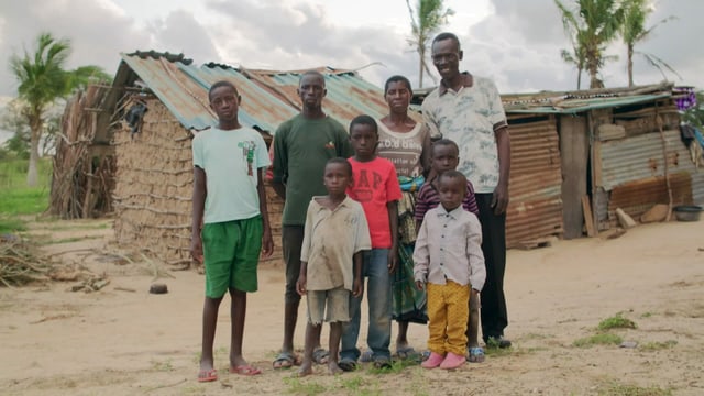 Eine Familie vor einem einfachen Haus mit Wellblechwänden. Eine Familie vor einem einfachen Haus mit Wellblechwänden.