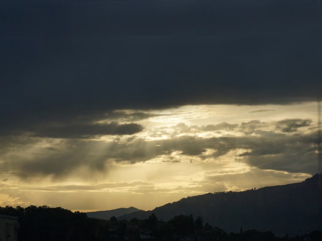 Am Himmel stehen dunkle Wolken. Dazwischen gibt es fahlgelbe Löcher und erste Sonnenstrahlen brechen hervor.