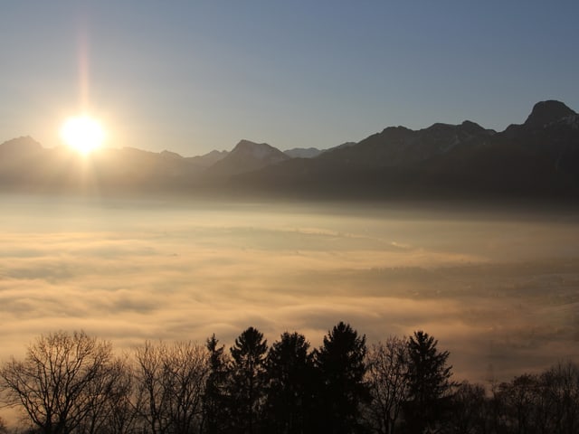 Die Sonne geht auf, hinter einer Bergkette. Im Vordergrund liegt das Nebelmeer.