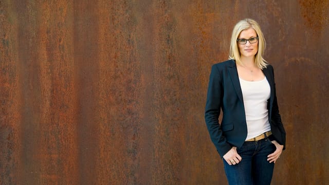 Eine Frau mit blonden Haaren steht vor einer rostigen Wand. Eine Frau mit blonden Haaren steht vor einer rostigen Wand.
