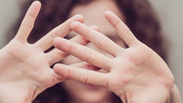 Eine Frau hält sich abwehrend die Hände vor das Gesicht Eine Frau hält sich abwehrend die Hände vor das Gesicht