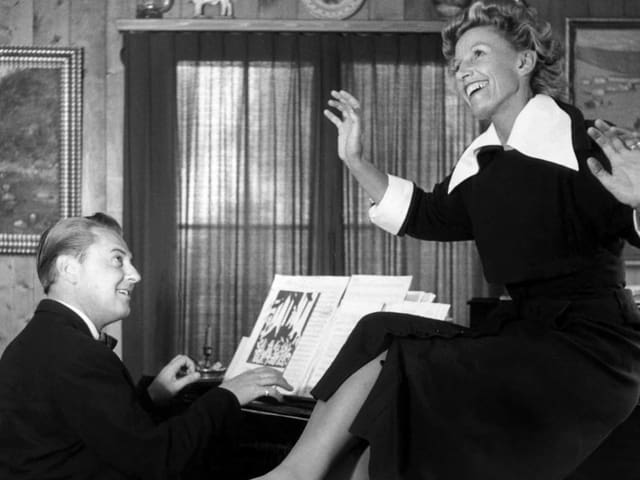 Frau sitzt auf Klavier auf dem ihr Mann ein Lied spielt. Frau sitzt auf Klavier auf dem ihr Mann ein Lied spielt.