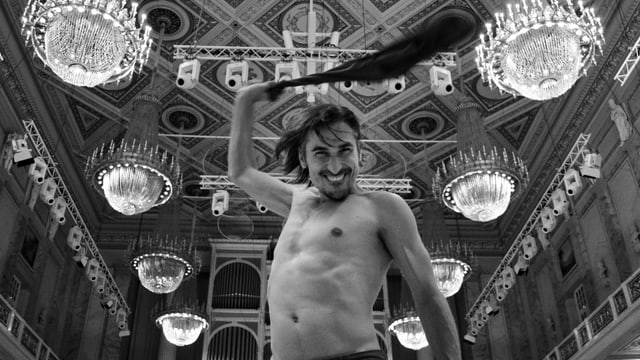 Ein Mann mit nacktem Oberkörper steht in einem Konzerthaus für klassische Musik. Ein Mann mit nacktem Oberkörper steht in einem Konzerthaus für klassische Musik.