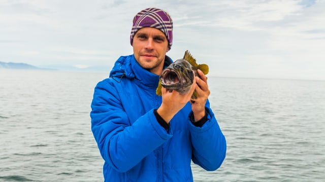 Ein Mann hält einen Fisch in die Kamera Ein Mann hält einen Fisch in die Kamera