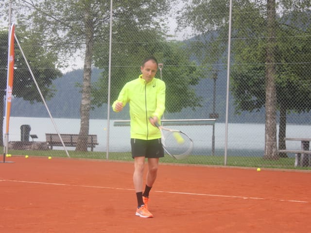 Mann in gelber Jacke spielt Tennis.