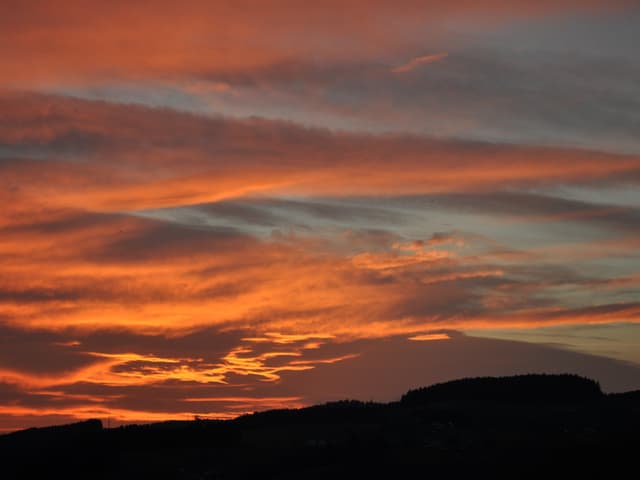 Der Himmel über Konolfingen scheint zu brennen. Die aufgehende Sonne taucht den bewölkten Himmel in Orange und Rot.