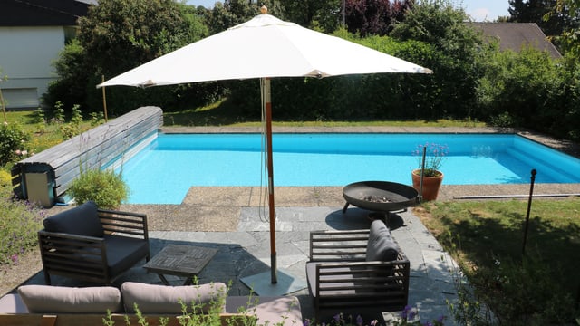 Ein Sonnenschirm an einem Gartenpool. Er gibt bei diesem Sonnenstand nur einem Sitzplatz Schatten. Ein Sonnenschirm an einem Gartenpool. Er gibt bei diesem Sonnenstand nur einem Sitzplatz Schatten.