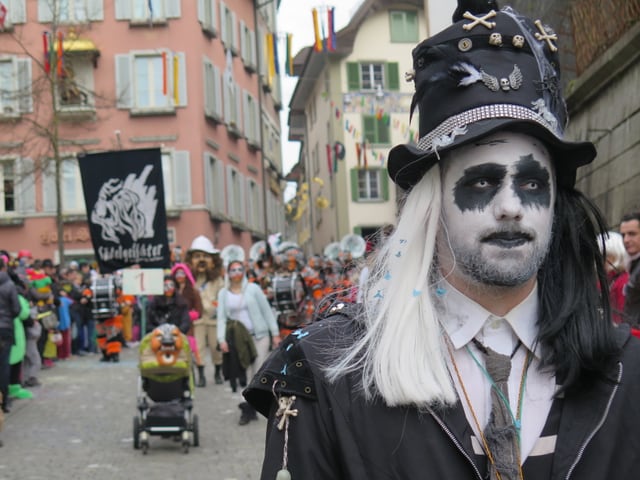 Geschminkte Figur, dahinter Umzugstart