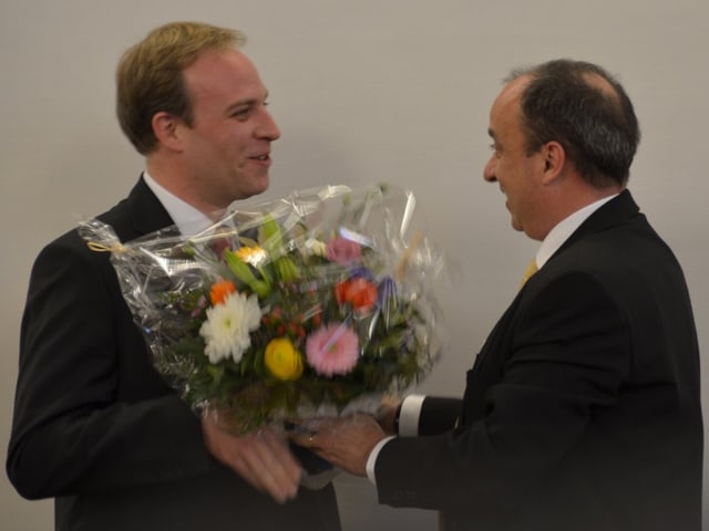 Mann überreicht anderem Mann einen Blumentstrauss und schüttelt die Hand Mann überreicht anderem Mann einen Blumentstrauss und schüttelt die Hand