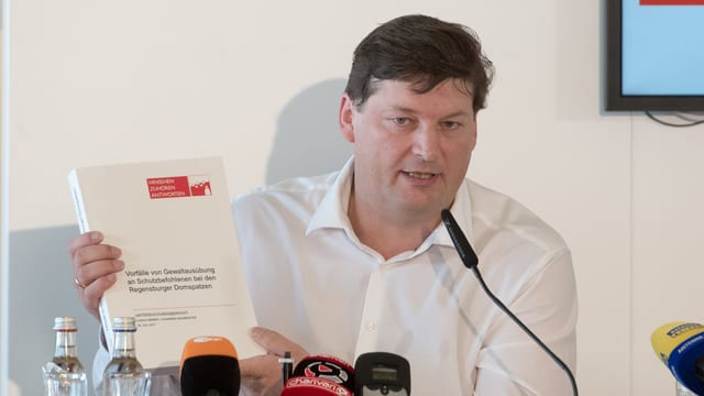 Mann mit Bericht in der Hand vor Mikrifonen Mann mit Bericht in der Hand vor Mikrifonen