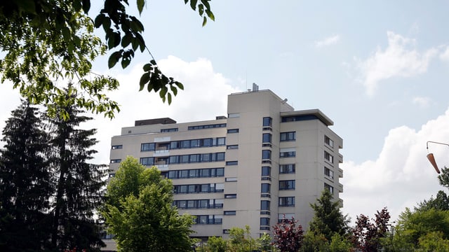 Ein Hochhaus in der Mitte des Bildes. Links und am unterern Bildrand grüne Bäume. Ein Hochhaus in der Mitte des Bildes. Links und am unterern Bildrand grüne Bäume.