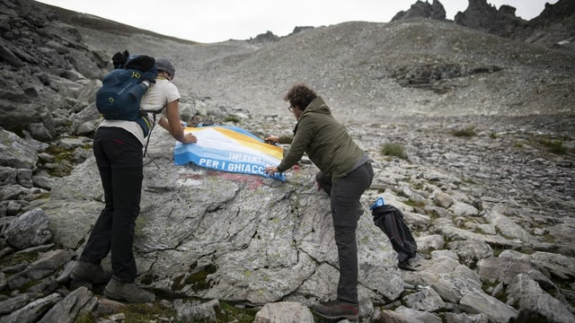 Zwei Männer legen eine Gletscher-Initiative-Fahne auf einen Felsen am Rand eines Gletschers