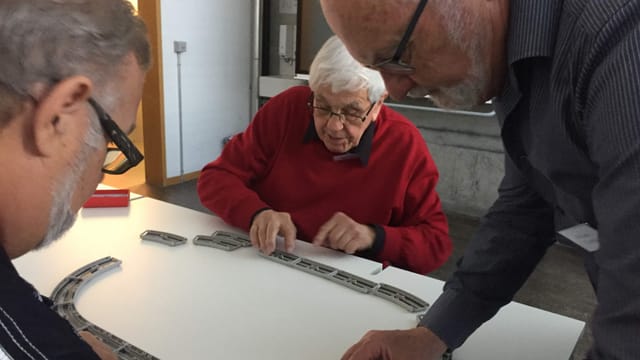 Ältere Menschen stehen um einen Tisch Ältere Menschen stehen um einen Tisch