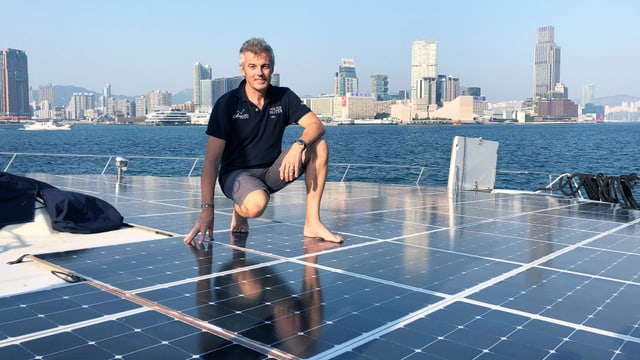 Ein Mann steht auf Solarpanels auf einem Katamaran. Ein Mann steht auf Solarpanels auf einem Katamaran.