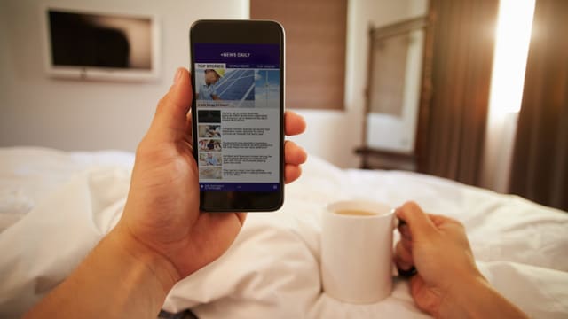 Ein Mann liegt im Bett und liest auf dem Smartphone die News. Ein Mann liegt im Bett und liest auf dem Smartphone die News.