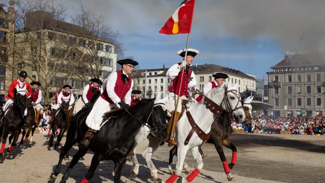 Zahlreiche Reiter umrunden dem Böögg mit der Standarte der Zunft Riesbach Zahlreiche Reiter umrunden dem Böögg mit der Standarte der Zunft Riesbach