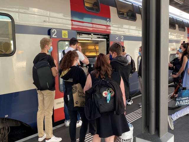 Menschen ziehen vor dem Einsteigen in den Zug eine Maske an