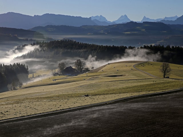 Blick in die Hügellandschaft des Emmentals. Zwischen den Hügel hat es Nebelfetzen. Darüber ist der Himmel wolkenlos.