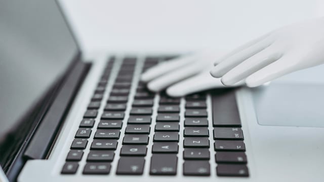 Eine Roboterhand liegt auf dem Keyboard eines Laptops Eine Roboterhand liegt auf dem Keyboard eines Laptops