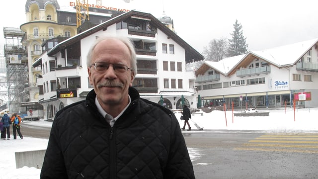 Ein Mann mit schwarzem Mantel, grauen Haaren und Brille auf einem verschneiten Trottvoir. Ein Mann mit schwarzem Mantel, grauen Haaren und Brille auf einem verschneiten Trottvoir.
