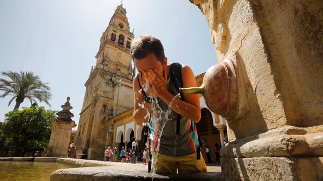 Mann benetzt sich das Gesicht an einem Wasserstrahl. Im Hintergrund ein Turm. Mann benetzt sich das Gesicht an einem Wasserstrahl. Im Hintergrund ein Turm.