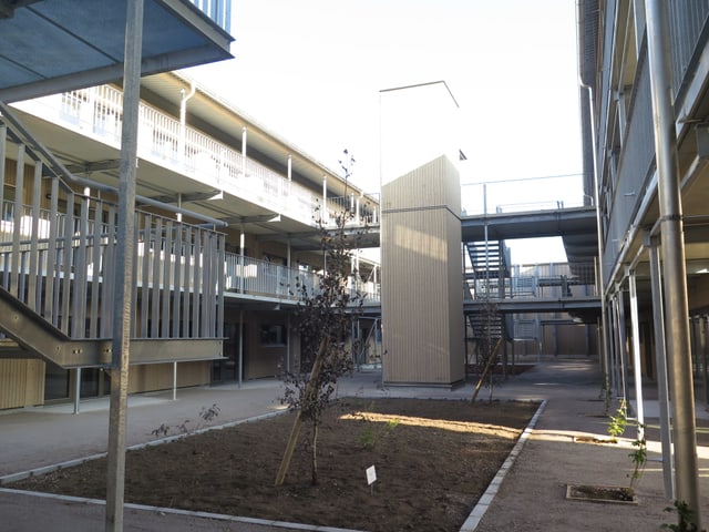 Blick in das Innere der neuen Siedlung Fogo. In der Mitte braune Erde, darum herum ein Holzbau mit Balkonen. Blick in das Innere der neuen Siedlung Fogo. In der Mitte braune Erde, darum herum ein Holzbau mit Balkonen.
