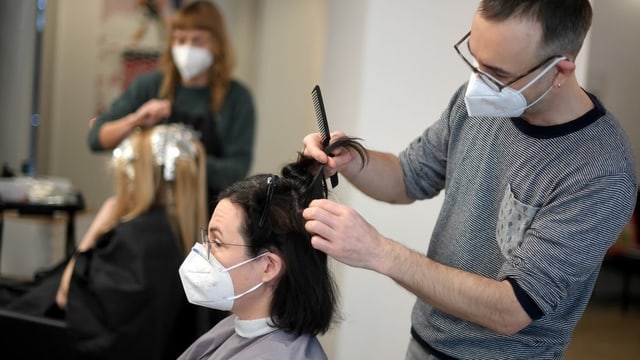 Coiffeur schneidet Frau die Haare. Beide tragen Maske. Coiffeur schneidet Frau die Haare. Beide tragen Maske.