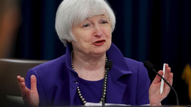 Janet Yellen in violett-blauem Deux-Pièce vor einem Mikrofon sitzend Janet Yellen in violett-blauem Deux-Pièce vor einem Mikrofon sitzend