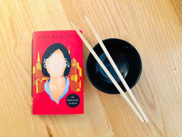«Kim Jiyoung geboren 1982» von Cho Nam-Joo liegt auf einem Tisch mit Schüssel und Essstäbchen daneben «Kim Jiyoung geboren 1982» von Cho Nam-Joo liegt auf einem Tisch mit Schüssel und Essstäbchen daneben