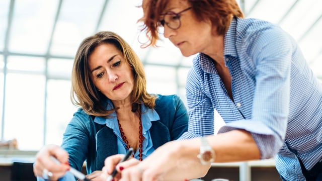 Zwei Frauen mittleren Alters arbeiten gemeinsam an einem Pult. Zwei Frauen mittleren Alters arbeiten gemeinsam an einem Pult.