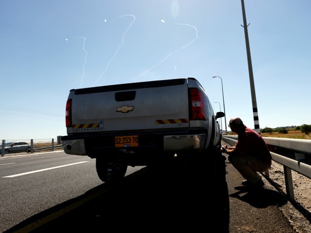 Ein Mann nimm hinter einem Auto Deckung bei einem Raketenangriff in Israel. Ein Mann nimm hinter einem Auto Deckung bei einem Raketenangriff in Israel.