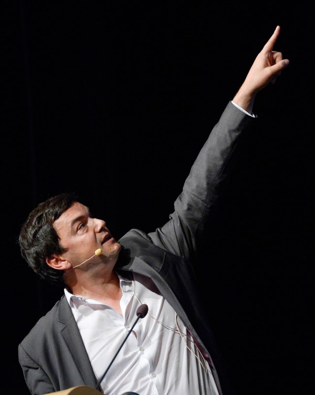 Piketty bei einem Vortrag, zeigt mit ausgestrecktem Arm auf einen Punkt auf einer nicht sichtbaren Leinwand Piketty bei einem Vortrag, zeigt mit ausgestrecktem Arm auf einen Punkt auf einer nicht sichtbaren Leinwand