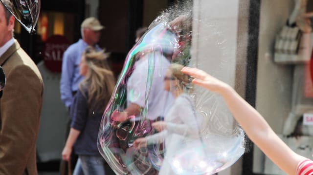Szene in einer Stadt: Eine Hand bringt eine grosse Seifenblase zum Platzen.