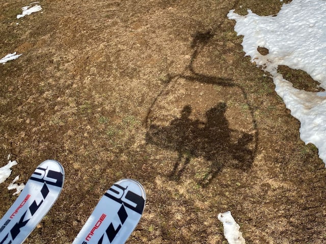 Skifahrer auf Sessellift vor aperer Wiese Skifahrer auf Sessellift vor aperer Wiese