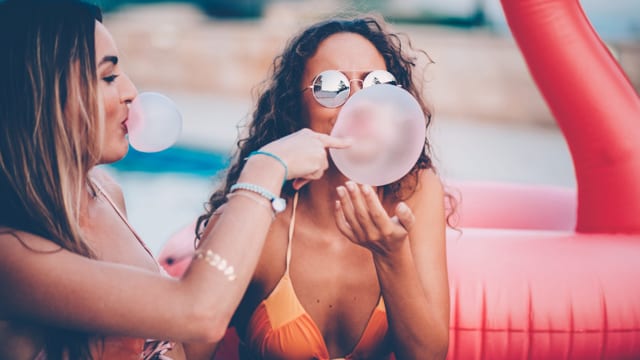 Zwei Frauen in Bikinis mit Kaugummiblasen. Zwei Frauen in Bikinis mit Kaugummiblasen.