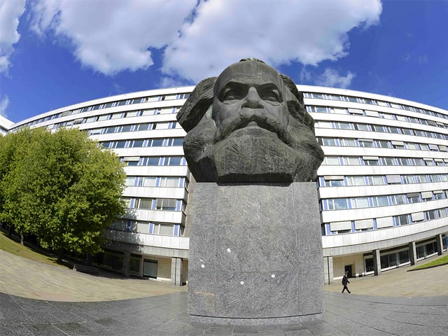 Karl-Marx-Statue, dahinter steht ein Gebäude.
