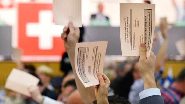 Mehrere Männer halten an der Versammlung der SVP weisse Wahlkarten in die Höhe, im Hintergrund eine Schweizer Flagge. Mehrere Männer halten an der Versammlung der SVP weisse Wahlkarten in die Höhe, im Hintergrund eine Schweizer Flagge.