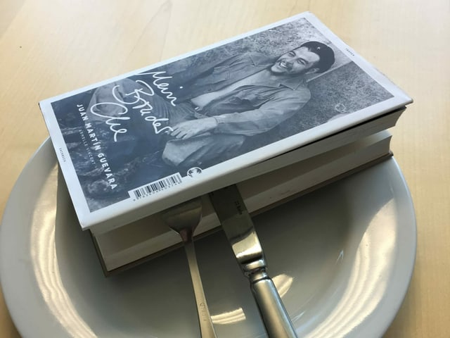 Das Buch «Mein Bruder Che» von Juan Martin Guevara liegt auf einem weissen Teller, das Besteck steckt mitten drin Das Buch «Mein Bruder Che» von Juan Martin Guevara liegt auf einem weissen Teller, das Besteck steckt mitten drin