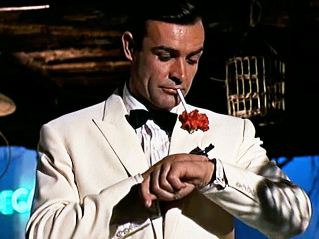 Bond im Anzug schaut auf seine Armbanduhr Bond im Anzug schaut auf seine Armbanduhr