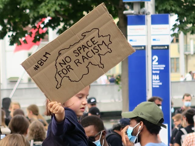 Ein Kind hält ein Plakat in die Höhe mit der Aufschrift: No space for racism – Kein Platz für Rassismus