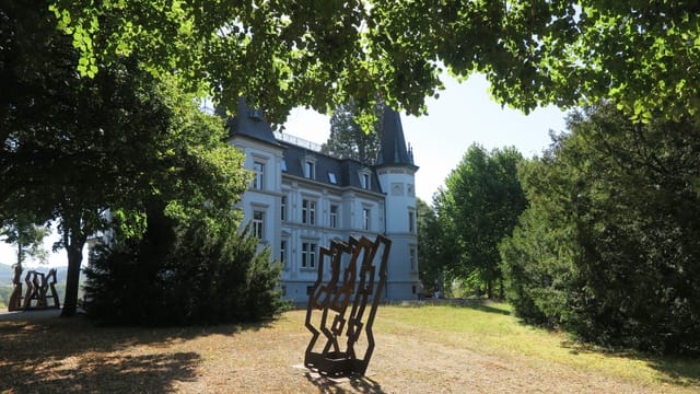 Skulptur aus Eisen auf einem Rasenfeld, dahinter grosse Villa Skulptur aus Eisen auf einem Rasenfeld, dahinter grosse Villa