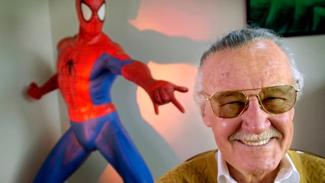 Stan Lee lachend im Bildvordergrund, hinten Spiderman-Puppe Stan Lee lachend im Bildvordergrund, hinten Spiderman-Puppe