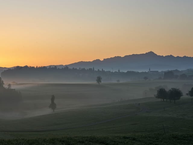 Nebelschwaden, die Sonne lugt hinter dem Bergpanorama hervor.